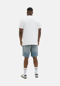 Hvid bomulds t-shirt, blå denim shorts med en falmet finish, hvide sokker og sorte sandaler. Synlig syning og baglommer på shortsene.