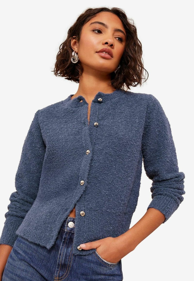 Adīta zila kardigāna ar strukturētu apdari, apaļu kakla izgriezumu un septiņām sudraba pogām priekšpusē. Ribota piedurkņu un apakšmalas apdare.