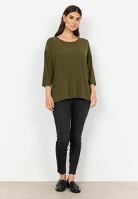 Olivno zelena, rebrasta pletiva bluza z ladijskim izrezom in rokavi do tri četrtine, povezana s črnimi prilegajočimi se jeans hlačami in črnimi loaferji.