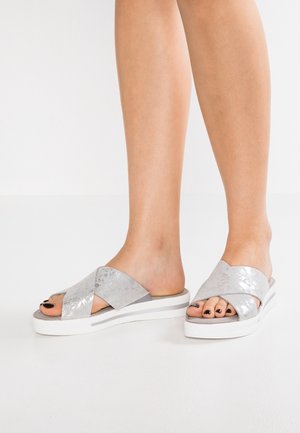 Sandales à glissière argentées croisées avec un motif texturé, semelle blanche et bout ouvert, sur fond blanc uni.