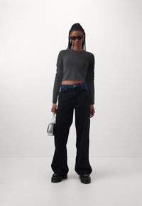 Cropped gray long-sleeve top, wide black jeans, chunky black shoes, and small silver handbag. Sleek design with a smooth texture.