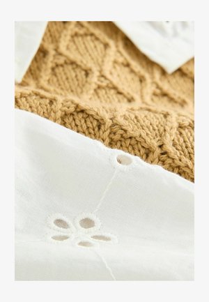 Un tessuto bianco texturizzato con dettagli in pizzo floreale sovrappone un tessuto dorato lavorato a maglia con un motivo a diamante, mostrando un netto contrasto nei materiali.