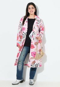 Lange roze jas met cartoon-stijl print, zwarte knopen, gecombineerd met een zwarte top en gescheurde blauwe jeans, accessoires met een gouden handtas.