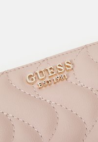 Lyserosa syntetisk lær lommebok med en quiltemønster, preget "GUESS"-logo i gull, og dekorativ søm.