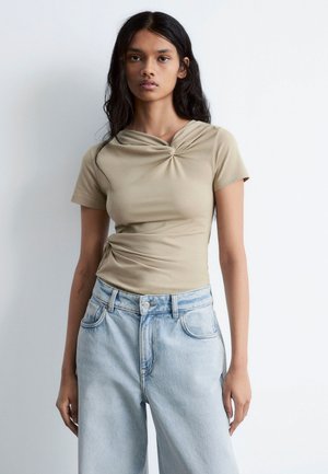 Beige short-sleeve top with a twisted neckline, paired with light blue high-waisted jeans. Smooth fabric with a fitted silhouette.
