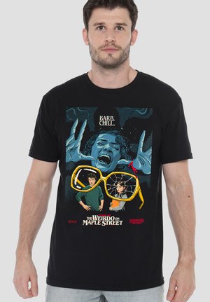 Man wearing a black Stranger Things T-shirt showing a screaming blue-toned face, large cracked yellow glasses, and two characters below with text.