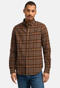 Button-up flanellen shirt in bruin met oranje en blauwe ruitpatronen. Beschikt over een kraag, lange mouwen en een afgeronde zoom. Zachte stoftextuur.