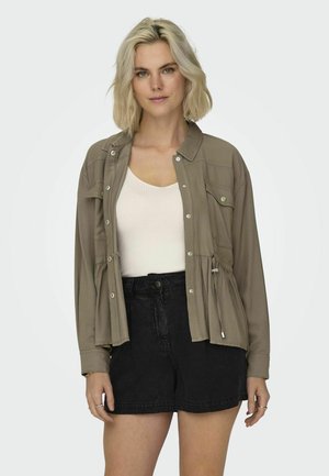 Light brown button-up jacket featuring a drawstring waist, chest pockets, and a relaxed fit, paired with black denim shorts.
