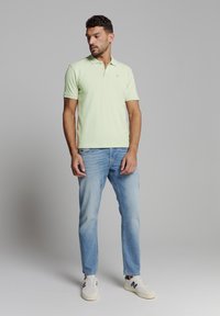 Lichtgroen polo shirt met korte mouwen, gemaakt van katoen, met een twee-knopenlijst. Gecombineerd met lichtblauwe jeans en witte sneakers met donkere accenten.