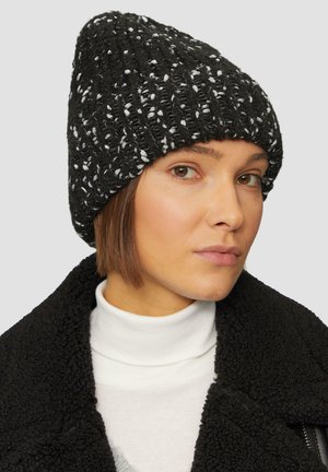 Bonnet en tricot noir avec un motif texturé et des accents blancs, coupe ajustée et légèrement pointue sur le dessus, associé à une veste en sherpa noire.