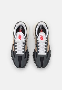 Grå och svarta sneakers med beige detaljer, texturerat tyg och framträdande snörning. Har en gummisula med distinkt mönster.