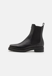 Sorte lær ankle boot med elastiske sidestykker, en lav stablet hæl og en pull tab på bagsiden. Glat tekstur og elegant design.