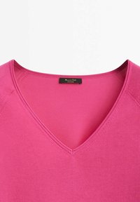 T-shirt rose à col en V, manches courtes, texture douce, avec une étiquette portant le nom de la marque. Tissu lisse et extensible avec une couture simple.