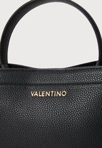 Fekete bőr kézitáska pehelykönnyű textúrával, arany "VALENTINO" logóval és strukturált dizájnnal. Két fogantyú a hordozáshoz.