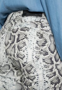 Jeans skinnies com um padrão de cobra em preto e branco. Feitos de denim, com um bolso traseiro e uma etiqueta de logo preta na cintura.