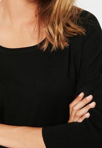 Maglietta nera a maniche lunghe con scollo ampio, maniche testurizzate e vestibilità aderente. Il tessuto sembra morbido ed elastico.
