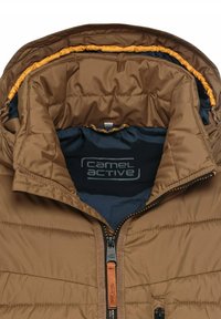 Brun pufferjakke med en kviltet tekstur, udstyret med lynlås, orange inderskud og et blåt brandlogo indeni kraven.
