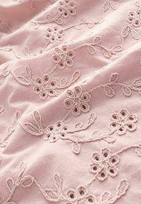 Tessuto rosa con ricami floreali. Presenta intricate fantasie floreali e disegni simili a vigneti in un filo più chiaro, creando un aspetto testurizzato.