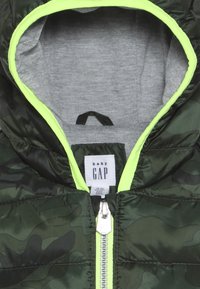 Zelená dětská bunda se vzorem maskáče, šedým vnitřkem a neonově zelenými detaily. Obsahuje přední zip a štítek s nápisem "baby GAP".