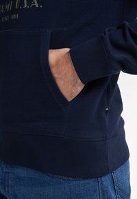 Tmavě modrá mikina s kapucí z bavlny, s přední kapsou, žebrovanými manžetami a lemem, jemnými šicími detaily a textem s logem.