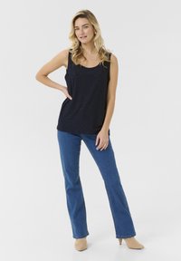 Merevaba navy sinise värvi ilma varrukateta topp, millel on aukudega muster, koos siniste laienevate teksade ja beeži kontsaga. Topp sisaldab ümarat kaelust ja külgmisi lõhikuid.