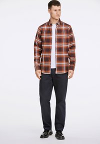 Camicia a quadri rossa e marrone con bottoni, indossata sopra una maglietta bianca. Abbina pantaloni navy e scarpe nere. Tessuto liscio, vestibilità casual.