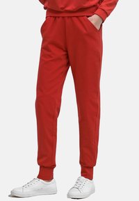 Røde sweatpants med elastisk talje og manchetter, med sidelommer og en glat stofoverflade. Sært med hvide sneakers.