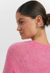 Pūkuotas rožinis megztinis su apvaliu kaklu ir raglano rankovėmis, lengva tekstūra ir subtiliais mezginiais.