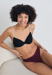 Black padded bra with white branded straps, paired with burgundy high-waisted underwear. Smooth fabric with seamless design.