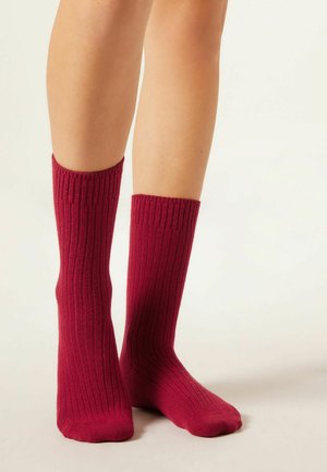 Chaussettes montantes à côtes de couleur bourgogne profond, fabriquées à partir d'un matériau doux, avec un ajustement serré en haut et une texture lisse tout au long.