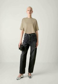 Beige cropped póló, magas derekú fekete farmer, ezüst mokaszin, és kis fekete kézitáska. Egyszerű dizájn, sima textúra, laza fazon.