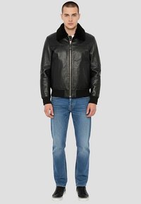 Veste en cuir noir avec col en fourrure, fermeture éclair et poignets côtelés. Associée à un jean bleu clair et des baskets noires.