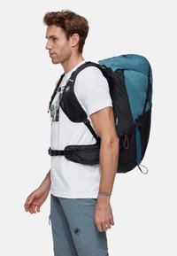 Plecak z niebieskimi i czarnymi sekcjami, regulowanymi paskami, siateczkowymi kieszeniami oraz pasem biodrowym. Wyposażony w zamocowania webbingowe i elegancki design.