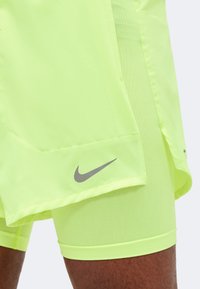 Shorts de sport jaune-vert vif superposés avec des shorts de course assortis, avec un petit logo Nike swoosh gris sur l'ourlet.