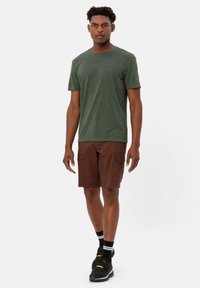 T-shirt a maniche corte verde scuro e pantaloni corti marroni con tasche cargo. Il modello indossa sneaker nere e calze rigate bianco e nero.