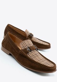 Mocasines de ante marrón con parte superior de tela a cuadros, que presentan un hebilla decorativa en tono plateado y acentos de costura. Suela antideslizante.
