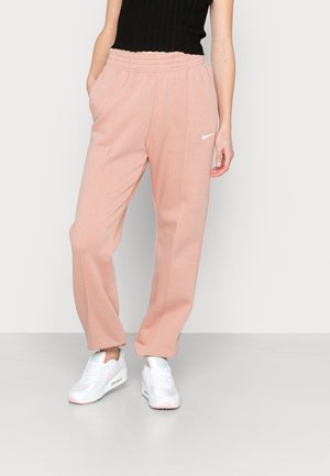 Vrouw draagt roze Nike joggingbroek met elastische tailleband en zijzakken, gecombineerd met witte sneakers en een zwart mouwloos topje.