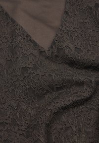 Musta pitsikangas, jossa on kukkakuvioita, kerrostettuna tummanruskean taustan päälle. Pitsi on hieno, herkkä rakenne ja monimutkainen yksityiskohtaisuus.