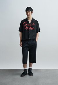 Μαύρο πουκάμισο με κουμπιά και κόκκινο κείμενο "Ανοιχτά 24 ώρες", συνδυασμένο με μαύρες σορτς μέχρι το γόνατο και μαύρα ψηλά sneakers. Μινιμαλιστικός σχεδιασμός.