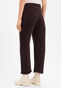 Pantalon en velours côtelé bordeaux avec une coupe décontractée et des revers roulés, doté de poches arrière et d'une fermeture à bouton à la taille.