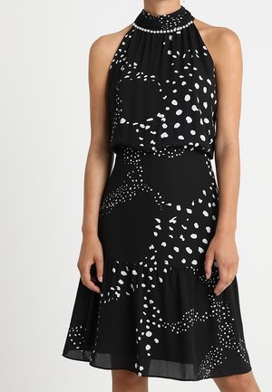 Robe noire sans manches avec des points abstraits blancs, col montant orné de perles semblables à des perles et jupe évasée.