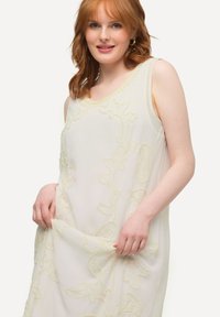 Vestido sin mangas en crema con bordados florales en amarillo suave. Tejido ligero y fluido con escote redondo y detalles intrincados.