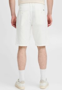 White shorts with a straight cut, made of lightweight material, featuring back pockets and turn-up hems, paired with white socks and shoes.