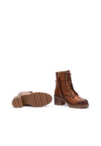 Botas de tobillo de piel marrón con un diseño de cordones, un cierre de cremallera lateral y un tacón grueso. Suela de goma texturizada con detalles de tracción.