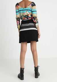 Långärmad topp i färgglad blommig och randig mönster, ihop med en svart kjol med texturerad midja och silverdetaljer. Svarta ankelboots.