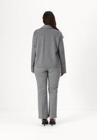 Grå rutete dress med skreddersydd blazer og rette bukser. Blazeren har krage og lange ermer; buksene er ankellange og bæres med hæler.