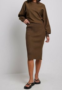 Brun stickad topp med överdimensionerade ärmar som är kombinerad med en brun ribbad pennkjol. Har en medellång design och platta sandaler.