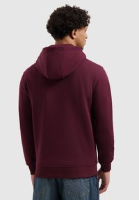 Bordeauxrode pullover hoodie met een capuchon met trekkoord, geribbelde manchetten en tailleband. Gladde stoftextuur, eenvoudig ontwerp, geen zichtbare patronen of logo's.