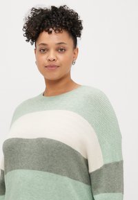 Pleten pulover v mehkih zelenih in kremnih črtah. Malce prevelik kroj z rebrasto teksturo in okroglo ovratnikom.