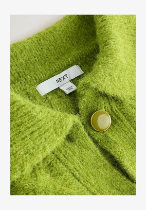Green knitted cardigan featuring a textured finish, large yellow button, and a label that reads "NEXT." Made in China.